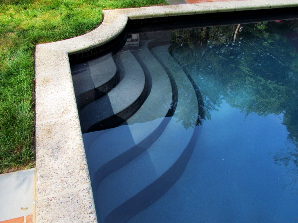An in-ground pool with a corner staircase, showcasing a deep, dark pool interior filled with water.