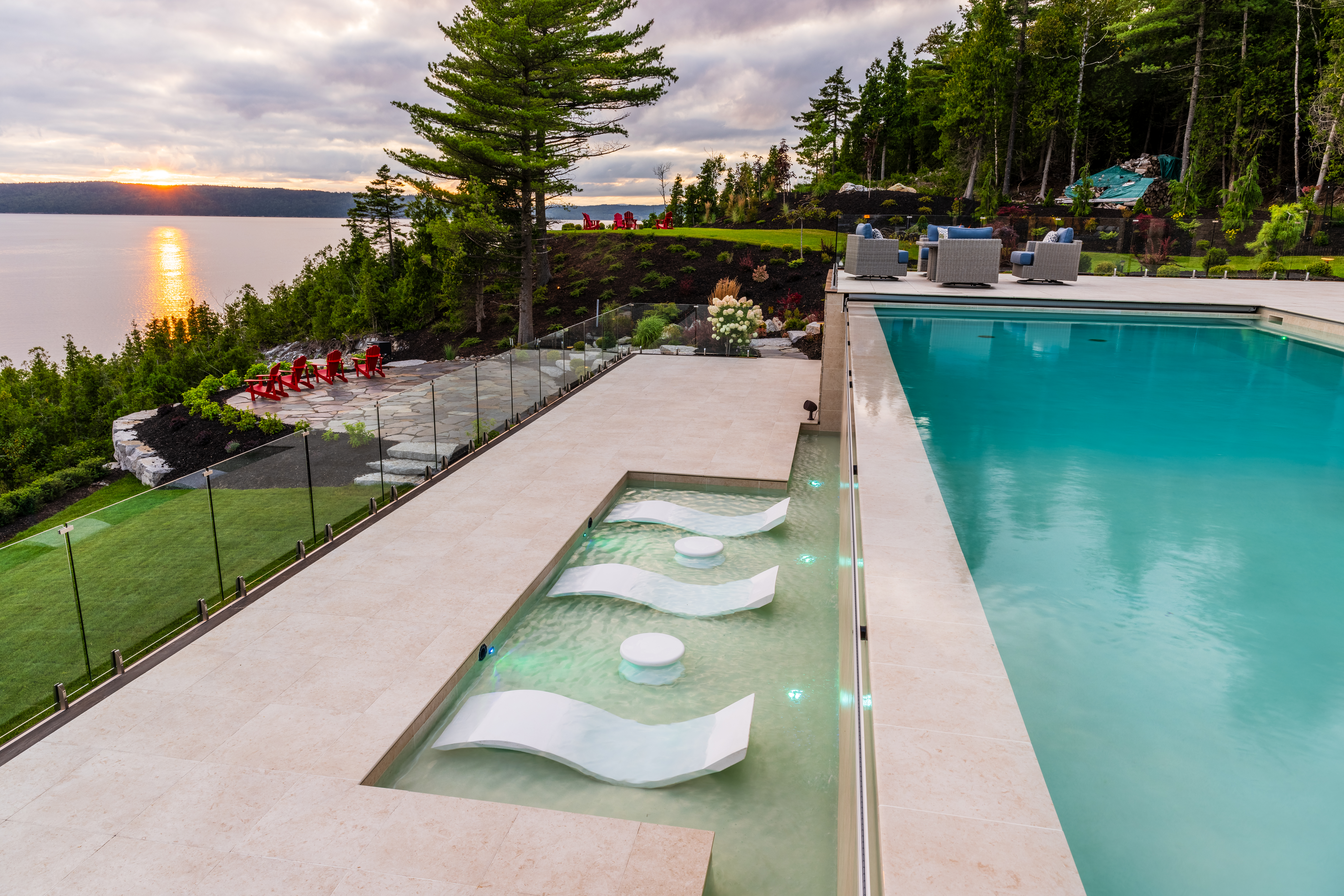 The sun sets on multi-level pool next to a large body of water.