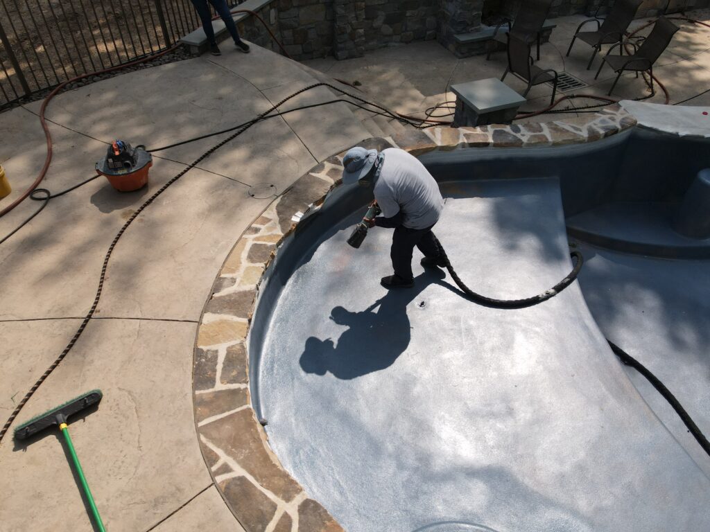 A worker is applying an ecoFINISH coating to an inground pool.
