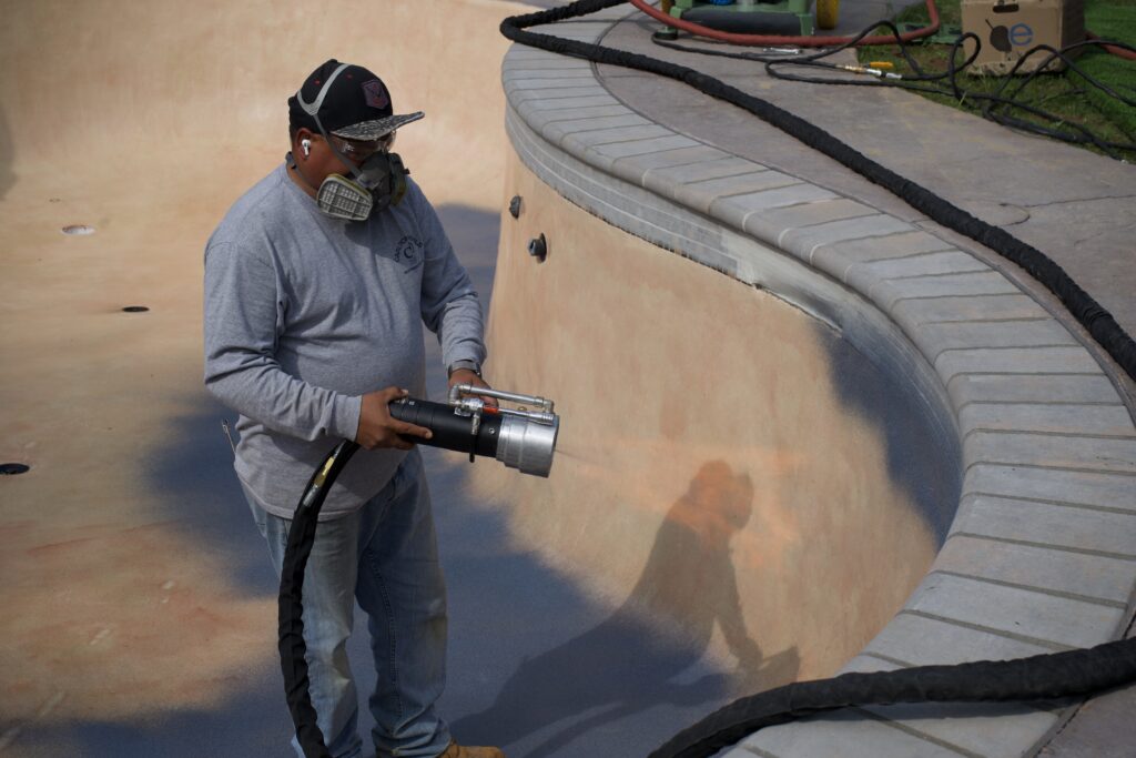 Worker wearing a mask and using a controlled flame for surface treatment on an in-ground pool.