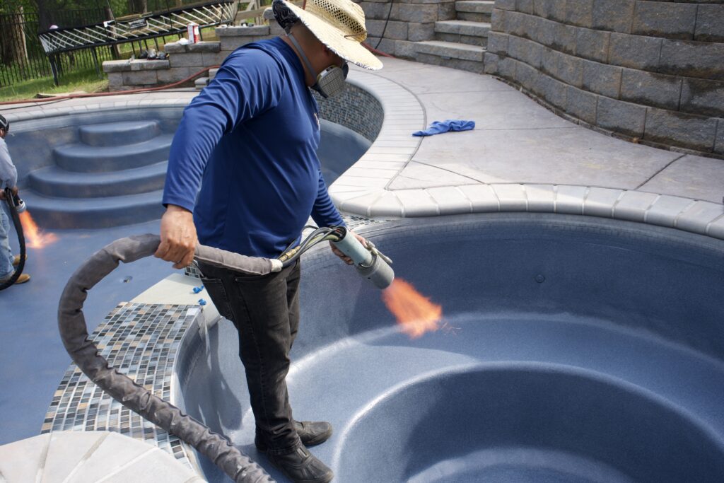 Workers using flames to treat the surface of an in-ground pool.
