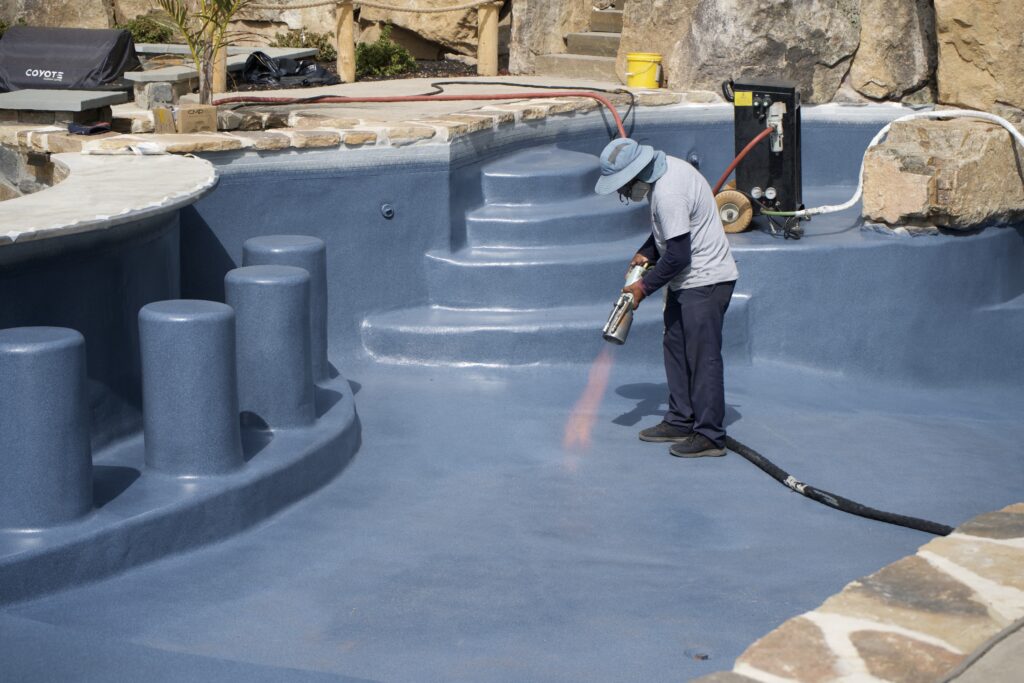 Workers using a flame to treat the surface of an in-ground pool.