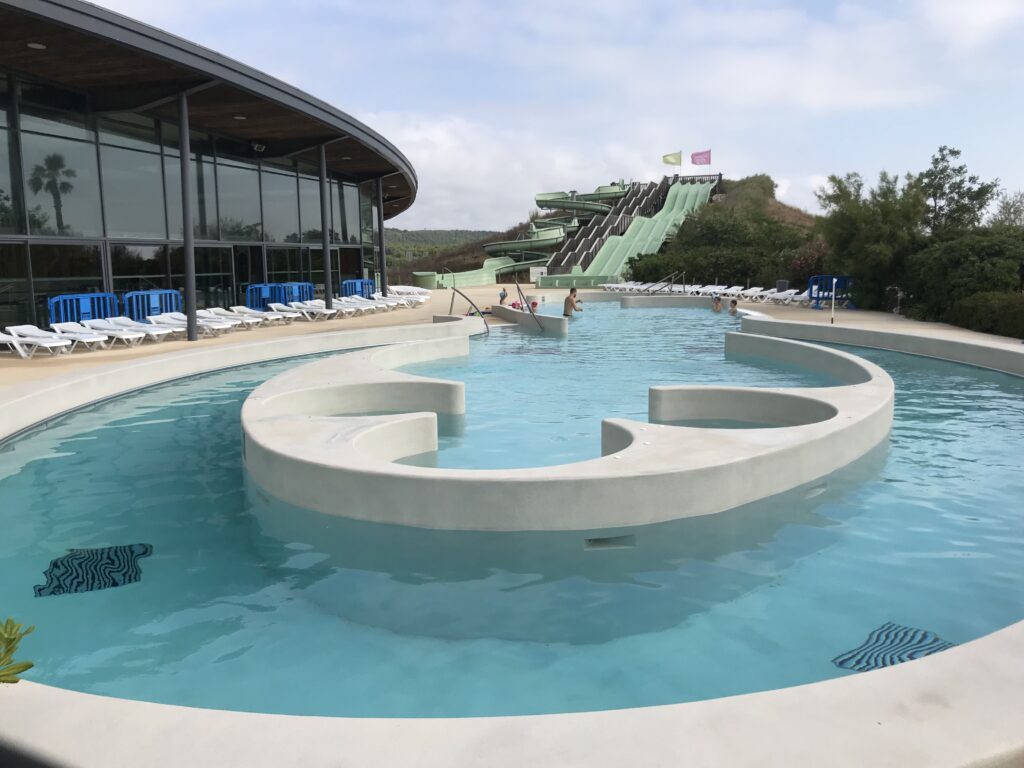 Expansive waterslides descending into a gently curved, shallow in-ground pool with swimmers.