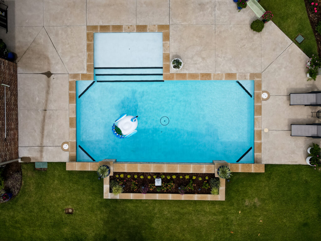 Overhead view of a backyard oasis featuring a rectangular pool and a whimsical blue bird floatation device.