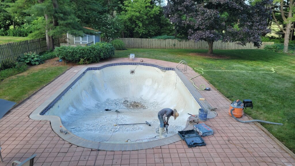 Worker inside an in-ground pool cluttered with debris.