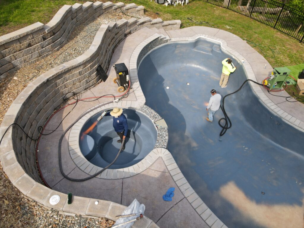 Overhead shot of workers using a weed burner to test the pool's surface temperature.